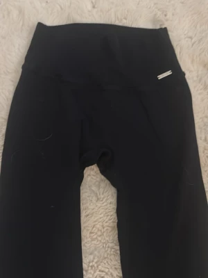 Svarta ribbade leggings från Aim'n - Säljer ett par svarta leggings från Aim'n med ribbad struktur och hög midja. De är stretchiga och sitter tajt, perfekta för träning eller chill. Metallogo på linningen ger en snygg detalj. Superbekväma och lätta att matcha med allt.