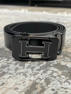 Läderbälte med automatiskt spänne – justerbar längd  - 📏 Storlekar: 130 cm & 135 cm Kan enkelt klippas i änden för perfekt passform.  🧵 Design: • Texturerat läder för en klassisk look • Slät läderfinish för en stilren, minimalistisk känsla (Bilder kan skickas vid intresse)  🔒 Automatiskt spänne: Smidigt klicksystem på insidan som sitter stadigt och enkelt justeras. Ger ett elegant och minimalistiskt uttryck.  🎨 Välj din logga: Flera loggor finns – välj din favorit. kolla min profil för alla alternativ 😊  📦 Snabb leverans 💬 Frågor? Hör av dig!