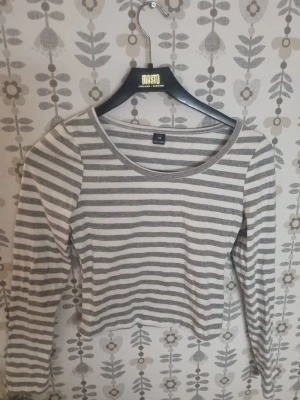 Randig croppad långärmad tröja XS - Snygg croppad långärmad tröja från Masto i storlek XS. Tröjan har ett klassiskt randigt mönster i grått och vitt, rund halsringning och mjukt bomullsmaterial som känns skönt mot huden. Perfekt för dig som gillar enkel och stilren design.