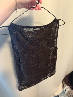 Svart spetsig ärmlös linnetopp - Säljer en svart ärmlös linnetopp med snygg spets och transparent känsla. Toppen har rund hals och är perfekt för dig som gillar en lite edgy och feminin stil. Spetsen ger en cool detalj och toppen är lätt att matcha med olika outfits.
