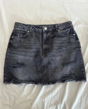 Svart jeanskjol från New Yorker -  svart jeanskjol i storlek XL. Köpte den förra året och bara använt en gång. Kjolen har en kort passform, slitna detaljer och fransad nederkant.