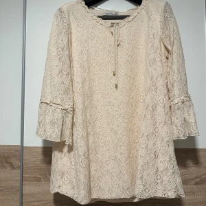 Beige spets cardigan från flash woman - Superfin beige kortklänning i spets från Saki Lora. Klänningen har trekvartsärmar med volangdetalj och snörning vid halsen. Perfekt för dig som gillar romantisk stil och mjuka färger. Spetsmönstret ger en extra touch av elegans och sommarkänsla.