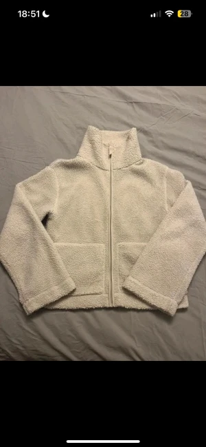 Vit teddyjacka med dragkedja - Mysig vit teddyjacka med hög krage och två stora fickor framtill. Jackan har en rak passform och stängs med dragkedja. Perfekt för dig som gillar chill och comfy stil. 