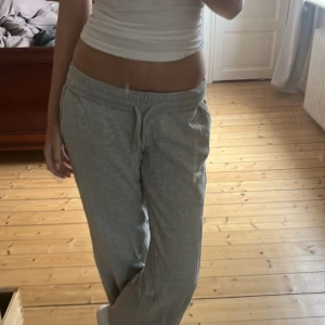 Lågmidjade Grå mjukisbyxor med snörning - Säljer ett par grå Lågmidjade mjukisbyxor med elastisk midja och snörning framtill. Byxorna har en loose passform och är tillverkade i mjukt bomullsmaterial, perfekta för chill dagar hemma eller när du vill vara extra bekväm. Enkla att matcha med en hoodie eller t-shirt. Innerbenslängden är 74cm, midjemåttet är 33cm men har stretch. Grenen är 23cm men om man viker ner (snöret syns endast om man viker ner) är grenen 19cm. 