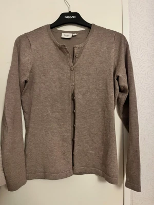 Beige kofta från Saint Tropez XS - Snygg beige kofta från Saint Tropez i storlek XS. Koftan har rund hals, långa ärmar och knappar hela vägen framtill. Materialet är mjukt och stickat, perfekt för lager-på-lager under höst och vinter. Enkel och stilren design som funkar till många outfits.