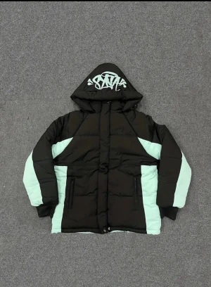 Svart och mintgrön pufferjacka med huva - Snygg pufferjacka i svart och mintgrönt med grafiskt tryck på huvan. Jackan har dragkedjor på fickorna och en cool färgblockad design. Perfekt för dig som vill sticka ut med streetstyle-vibe och hålla dig varm. Oversized passform och fodrad huva.