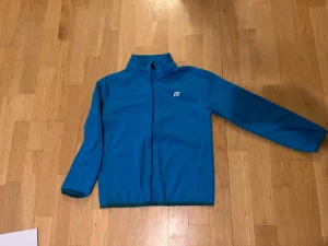 Blå fleecetröja från Everest - Blå fleecejacka från Everest med hel dragkedja och ståkrage. Jackan har långärmade ärmar och en enkel, sportig design med liten logga på bröstet. Perfekt för att hålla värmen under kyliga dagar.