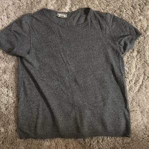 Mörkgrå stickad kortärmad tröja - En enkel och stilren mörkgrå stickad tröja från rund hals och korta ärmar. Tröjan har ribbade kanter vid ärmslut och nederkant. Stl S och använd fåtal gånger 💕