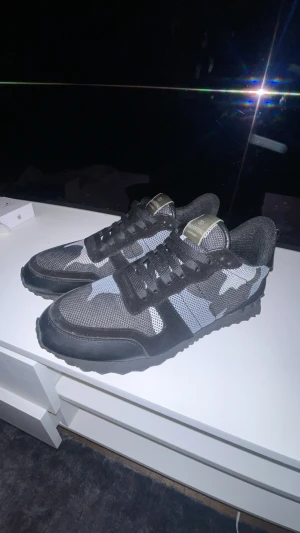 Valentino Rockrunner sneakers svart/grå - Snygga Valentino Rockrunner sneakers i svart och grått med camouflagemönster. Skorna har snörning, platt sula och detaljer i mesh och mocka. Perfekta för dig som gillar streetstyle och exklusiva märken.
