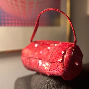 Röd paljettväska - Liten och söt aftonväska med glittrande paljetter över hela ytan. Insidan är fodrad med röd satin, stängs med dragkedja. Liten innerficka med dragkedja för små ting. Piffar upp vilken look som helst med lite extra bling, inte bara till jul och nyår…