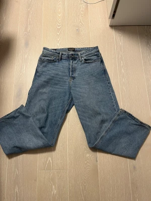 Blå baggy jeans från Jack & Jones - Säljer ett par klassiska blå jeans från Jack & Jones i baggy fit. Modellen har fem fickor, raka ben och normal midja. Jeansen är tillverkade i slitstarkt denim med snygga kontrastsömmar och passar dig som gillar en avslappnad stil.