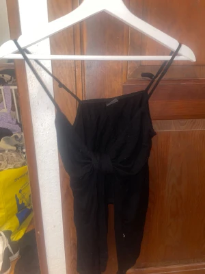 Svart tröja med knyt från Gina Tricot - Svart tröja från Gina Tricot i storlek S. Tröjan har smala axelband och en snygg knytning framtill som ger en cool och trendig look. Passformen är normal och materialet känns mjukt och bekvämt mot huden. Perfekt för dig som gillar stilrena och enkla plagg.