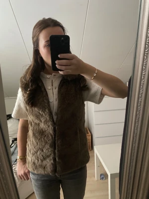 Brun pälsväst från Zara Girls  - Säljer en fluffig brun pälsväst från Zara Girls  med dragkedja framtill. Västen är i syntetpäls och har en mjuk insida, perfekt för att ge extra värme under kalla dagar. Enkel och stilren design som är lätt att matcha med olika outfits. aldrig använd 