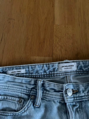Ljusblå loose fit jeans Jack & Jones - Säljer ett par ljusblå jeans från Jack & Jones i loose fit-modell Chris. Klassisk femficksdesign, raka ben och normal midja. Jeansen är tillverkade i mjukt denimtyg och har snygga detaljer som metallknapp och bälteshällor.