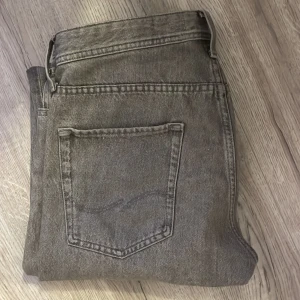 Grå jeans  - Säljer ett par grå jeans i rak passform med klassisk femficksdesign från Jack and Jones. Skick 9/10. W32 L30. Skriv vid minst fundering och pris kan diskuteras vid snabb affär!