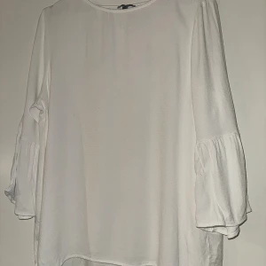 Vit blus med volangärm från Street One - Säljer en vit blus från Street One i storlek 42. Blusen har rund halsringning och långa ärmar med snygga volangdetaljer. Materialet är mjukt och lätt, tillverkat av viskos och elastan.