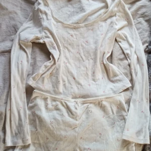 Vita blommiga pyjamas med spetskant - Säljer ett söt pyjamas set från H&M med små rosa blommor och diskreta ränder. Shortsen har en mjuk spetskant i midjan och är gjorda i tunn, skön bomull. Perfekta för varma dagar eller som mysplagg hemma.