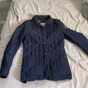 Mörkblå quiltad jacka från Lexington - Snygg mörkblå quiltad jacka från Lexington med klassisk krage, rikigt fräsch jacka som ger en stilren oxh Grisch look. Storlek S. Det enda negativa är att en av knapparna har gått sönder men det syns inte när man har den på. 