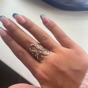 Silvrig blomformad ring - Silver ring i blomliknande design. Töjbar från en butik i Spanien (vet ej va de heter)