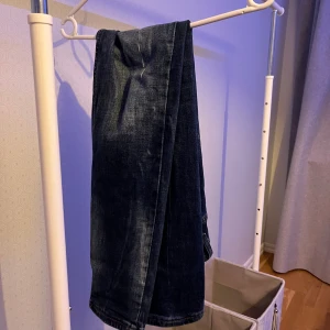  mörkblå jeans med slitningar - Säljer ett par mörkblå jeans från Dsquared2 med coola slitningar och detaljer. Jeansen har raka ben, klassisk femficksdesign och gröna sömmar vid fickorna. Märkespatch med tigrar bak i midjan. Perfekt för dig som gillar streetstyle. Passar dig tills du är upp till 175-180cm. Priset går att diskutera 