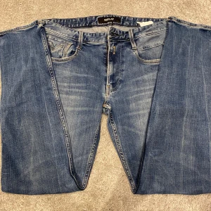 Replay Anbass Jeans - Snygga blå jeans från Replay med klassisk femficksdesign. Jeansen har en diskret tvättad look, Replay-logga på bakfickan och svart patch i midjan. Perfekta för dig som gillar en tidlös och avslappnad stil.