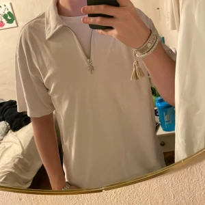 Vit pikétröja med dragkedja från H&M - Vit pikétröja från H&M i relaxed fit med kort ärm och halv dragkedja framtill. Dragkedjan har en snygg detalj med palmberlock. Perfekt för en chill och stilren look. Materialet känns mjukt och bekvämt mot huden. Använd någon gång så skicket är 10/10! Sitter perfekt på dig som vill ha lite större i armarna och riktigt skön tröja! Sitter bra på längden om man är runt 180 o uppåt 