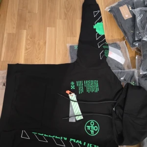 Svart hoodie Off-White med grönt tryck finns i alla storlekar - Finns även i olika storlek från S M L XL  hör av er för mer info…Svart hoodie från Off-White med gröna och vita grafiska tryck på bröst, rygg och ärm. Klassisk huva, känguruficka och coola detaljer som snörning och tydliga loggor. Materialet är mjuk bomull, perfekt för en streetwear-look.