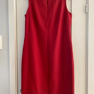 Röd ärmlös klänning från Ann Taylor Loft - Snygg röd klänning från Ann Taylor Loft med rund halsringning och ärmlös design. Klänningen är i en rak, enkel modell och har dragkedja bak.   Endast använd en gång och är i nyskick. Tyvärr finns det ett litet minimalt hål på klänningen.   Mått  Över bröstet: ca 50 cm  Över höften: ca 52 cm  Total längd från axeln och ner: ca 102 cm   Yttre tyget: 52% polyester, 43% ull och 5% lycra Underklänning: 100% acetate   Kommer från ett djur och rökfritt hem 