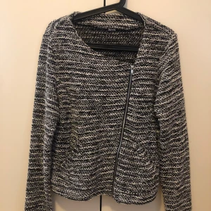 Svartvit stickad cardigan jacka - Snygg svartvit stickad cardigan jacka med lång ärm och asymmetrisk dragkedja framtill. Jackan har ett melerat mönster och är perfekt för lager-på-lager-stil. Passar dig som gillar en avslappnad men trendig look.