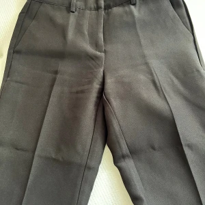 Svarta kostymbyxor från Nelly - Svarta kostymbyxor från Nelly med raka ben och pressveck. Byxorna har hällor för bälte, sidfickor fram och fuskfickor bak. Snygg passform. 