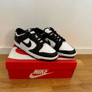 Nike Dunk Low Panda svart/vit - Nike Dunk Low Panda i svart och vitt skinn med klassisk låg siluett. Snygg kontrast mellan svart och vit, med svart swoosh och snörning. Perforerad tåbox för extra andningsförmåga och bekväm platt sula. Perfekta sneakers för dig som gillar stilrena och tidlösa färger. Självklart äkta.      Storlek 43. Helt nya! 