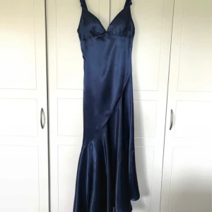 Marinblå långklänning i satin - Snygg marinblå långklänning med v-ringad urringning och breda axelband. Klänningen har en asymmetrisk skärning och är tillverkad i glansigt satinmaterial som ger en lyxig känsla. Superfin, perfekt för bal eller bröllop! Nypris är 1160kr, klänningen är oavnänd pga fel storlek💕