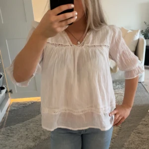 Vit blus - Säljer en luftig vit blus med v-ringning och fina spetsdetaljer vid bröstet och nederkanten. Blusen har trekvartsärm med lätt puff och är tillverkad i ett tunt, skönt material som ger en avslappnad och fräsch look. Köpte den från gina Young och endast använd en gång. 