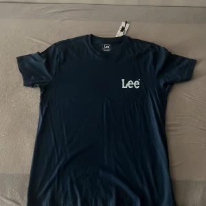 Mörkblå t-shirt från Lee i bomull - Snygg mörkblå t-shirt från Lee med vit logga på bröstet. Klassisk rund halsringning och regular fit. Tillverkad i mjuk bomull som känns skön mot huden. Perfekt för en clean och stilren look.