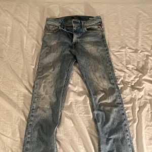 Replay ljusblå jeans Thad - Säljer ett par ljusblå jeans från Replay, modell Thad. Jeansen har klassisk femficksdesign, snygga slitningar och kontrastsömmar. Bakfickorna har broderad detalj och läderpatch med Replay-logga. Perfekta för dig som gillar en avslappnad och trendig look.