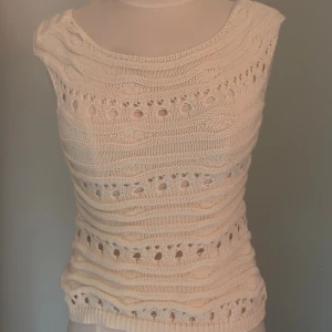 Stickad ärmlös topp i beige - Säljer en stickad ärmlös topp i beige med vågiga strukturer och hålmönster. Toppen har rund halsringning och är figurnära. Perfekt för dig som gillar en bohemisk och chill stil.