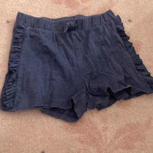 Mörkblå shorts med volangdetaljer ✨💙✨ - Supersöta mörkblå shorts med volanger längs sidorna och bekväm resår i midjan. Mjukt bomullsmaterial och snörning framtill gör dem perfekta för varma dagar. Snygga och enkla att matcha till din favorit-topp. 💙💙💙