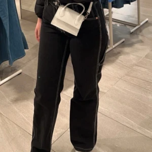 Svarta jeans med kontrastsömmar - Svarta jeans med vita kontrastsömmar och raka ben. Byxorna har hög midja, klassiska fem fickor och detaljerade sömmar längs benen och bakfickorna. 