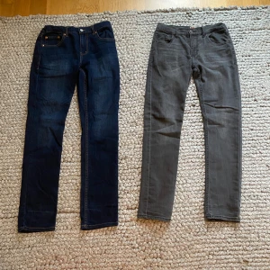 Levi's 512 Slim Taper jeans blå & grå - Två par Levi's 512 Slim Taper jeans säljes, ett par i mörkblå denim och ett par i grått. Båda har klassisk femficksdesign, smal passform och avsmalnande ben. Snygga kontrastsömmar på det blå paret. Perfekta för dig som gillar stilrena och moderna jeans.