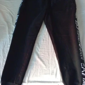 Svarta EA7 Emporio Armani mjukisbyxor - Svarta mjukisbyxor i stl S eller M från EA7 Emporio Armani med vit logga längs sidorna. Byxorna har en rak passform och är tillverkade i mjukt material som passar perfekt för en avslappnad stil. Snygga detaljer med tydlig branding längs benen. 