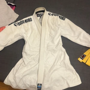 En hel vit gi med tryckning, ett par byxor från KWON och ett gult bälte. Kan köpas enskilt också - Säljer en vit judo/bok gi med byxor   från KWON, perfekta för kampsport som karate, Bjj, Jj eller judo. Byxorna har resår i midjan med snörning för skön passform och är tillverkade i en slitstark bomull/polyester-blandning. Klassisk rak modell utan mönster. Med ett helt nytt gult bälte 