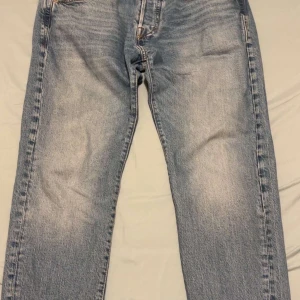 Blå jeans från Jack & Jones 30/34 - Snygga ljusblå jeans från Jack & Jones med klassisk femficksdesign och raka ben. Jeansen har en normal passform och är tillverkade i slitstarkt denim med subtila slitningar för en cool look. Perfekta för dig som gillar enkel och tidlös stil. Storlek 30/34, speciell model.