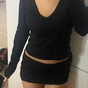 Svart ribbad v-ringad tröja - Svart långärmad tröja med v-ringning och ribbad struktur. Modellen är något croppad och har en enkel, stilren look som passar perfekt till jeans eller kjol. Mjuk och stretchig, perfekt för lager-på-lager under höst och vinter.