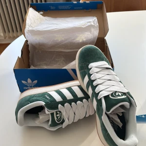 Adidas Campus mocka - Säljer ett par gröna Adidas Campus sneakers i mocka med klassiska vita ränder och vit sula. Skorna är endast testade på men passa ej så får därav sälja. Nypris i butiken är 800-1000 kr men mitt pris är förhandlingsbart. Storleken enligt bilden och det är bara att höra av sig vid funderingar🤗💸