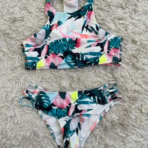 Färgglad blommig bikini - Superfin oanvänd bikini med tropiskt blommönster från stadium. Överdelen har hög hals och cutouts i sidorna, och underdelen har matchande banddetaljer på höfterna. 