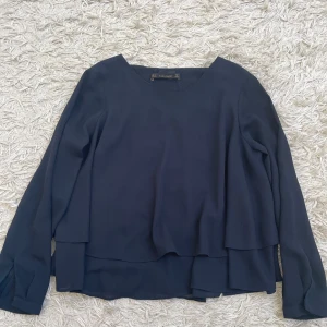 Marinblå blus  - Säljer en stilren marinblå blus från Zara Basic i storlek S. Blusen har långa ärmar, rund halsringning och dubbla lager som ger en snygg, flowy look. 
