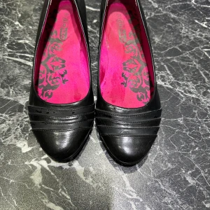 Svarta kilklackar från Din Sko - Svarta pumps från Din Sko med kilklack och rund tå. Skorna har dekorativa sömmar framtill och en snygg rosa innersula med svart mönster. 