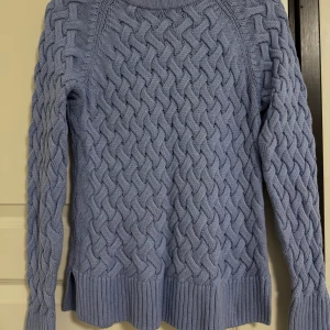 Ljusblå stickad tröja från C - Superfin ljusblå stickad tröja från C i storlek XS. Tröjan har ett chunky flätmönster över hela och breda ribbade muddar vid ärmslut och nederkant. Perfekt för dig som gillar en mysig och trendig look.
