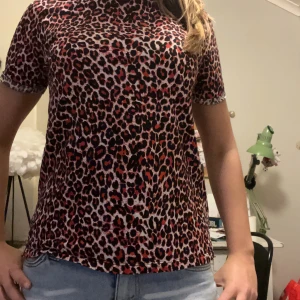 Supercool t-shirt!! - Säljer en snygg topp med leopardmönster i svart, rött och beige. Modellen har korta ärmar och rund hals, och är i en normal passform. Materialet känns mjukt och stretchigt, troligen polyester. Perfekt för dig som gillar djurmönster och vill sticka ut.