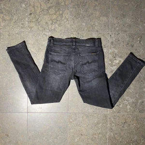 Nudie jeans - Säljer ett par svarta/gråa skinny jeans från Nudie Jeans i storlek 31/30. Jeansen har klassisk femficksdesign, svarta sömmar och Nudie-loggan på bakfickorna. Priset kan diskuteras!